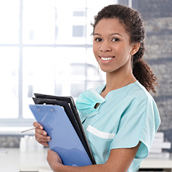 Smiling nurse in blue scrubs holding an armful of clipboards