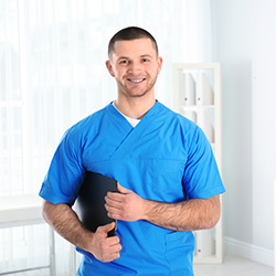 Smiling male nurse wearing blue scrubs and standing in a hallway